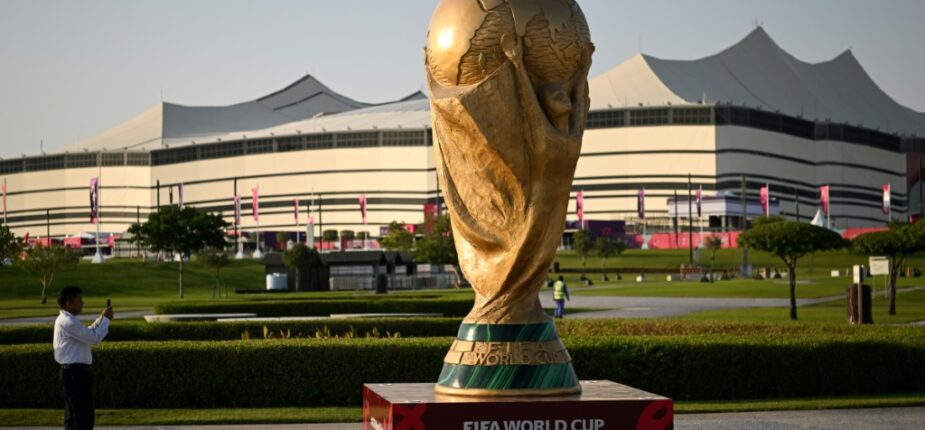 Un homme prend une photo d'une réplique géante du trophée de la Coupe du monde de football de la FIFA devant le stade Al-Bayt de al-Khor (Qatar) le 10 novembre 2022