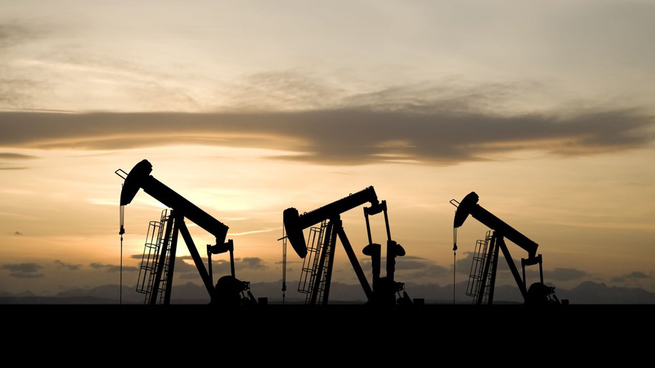 Three oil and gas industry derricks work as the sun sets behind them.